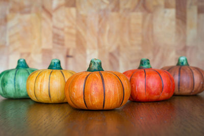Colourful ceramic pumpkins lined up on a wooden table with light brown wooden board in a background