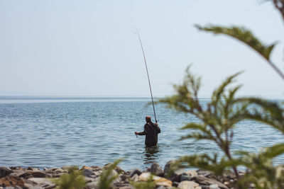 Man fishing in sea against clear sky