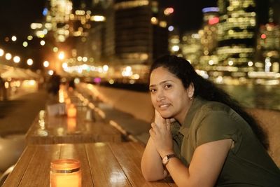 Portrait of woman sitting in illuminated city at night