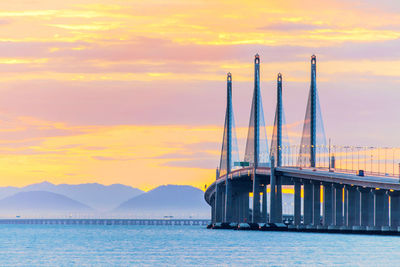 Bridge over sea against sky during sunset