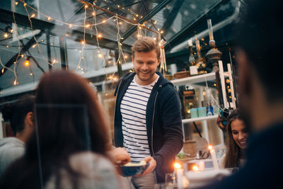 Smiling young man offering fruits to friends in glass cabin