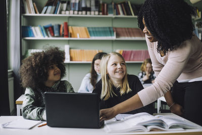 Boy and girl looking at teacher while doing e-learning in classroom