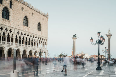 Blurred motion of people walking by building against sky