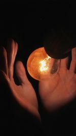 Close-up of hand holding illuminated candle against black background