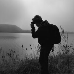 Silhouette man photographing at camera against sky