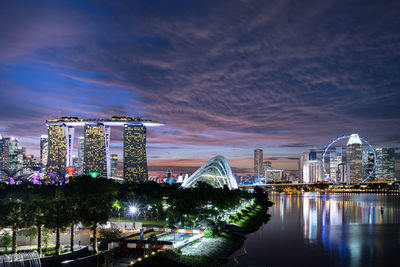 Illuminated buildings against cloudy sky at night