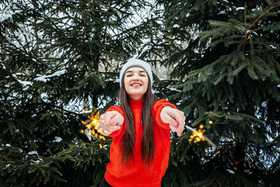 Outdoor portrait of happy cute latina girl in winter hat and red sweater posing with sparkler