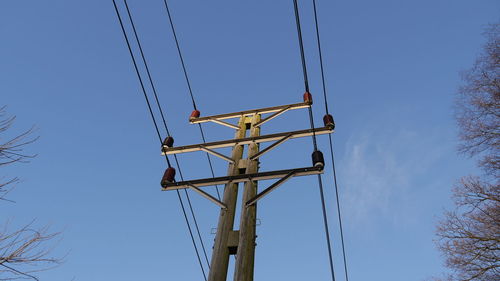 A electricity pylon with cables is seen, looking up from below. blue sky background. trees to side.