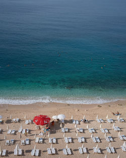 Beautiful empty beach with white chairs and red beach umbrella near very clear blue green ocean/sea