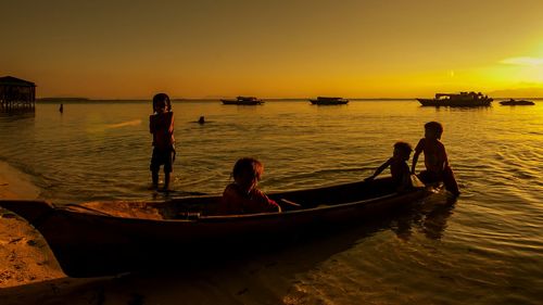 Silhouette people on shore against sky during sunset