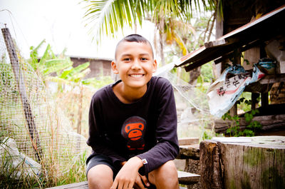 Portrait of smiling boy sitting on bench in yard