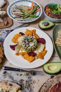 From above of dish of bean with petals on plate near fork with knife and pizza on table