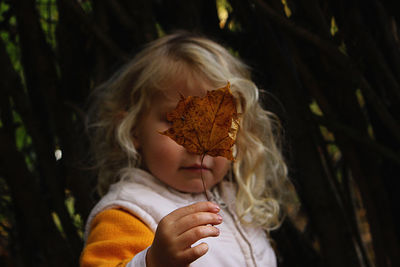 Close-up of cute girl holding leaf standing outdoors