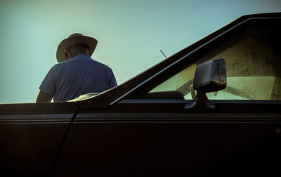 Portrait of adult man in cowboy hat standing against a vintage car during sunset