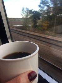 Close-up of hand holding coffee cup against sky