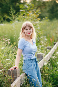 Portrait of smiling young woman leaning on fence by plants