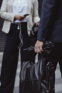 Midsection of businessman holding bag and umbrella while standing in city