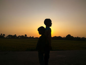 Silhouette man standing on field against sky during sunset