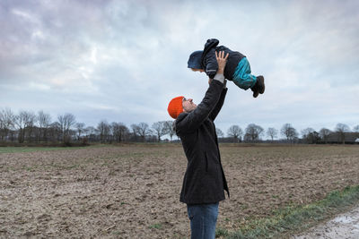 Side view of father lifting daughter on field during winter