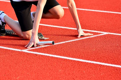 Low section of athlete holding relay baton while kneeling on starting line