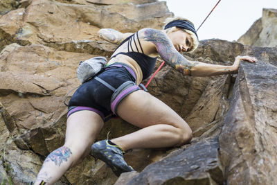 Tattooed girl rock climbing with friend on summer day