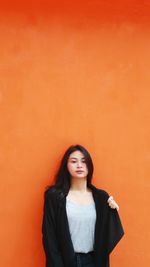 Portrait of young woman standing against orange wall