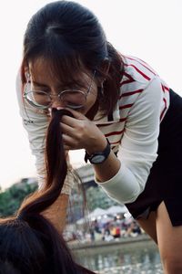 Young woman smelling hair of friend against sky