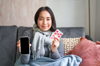 Portrait of young woman using mobile phone while sitting on sofa at home