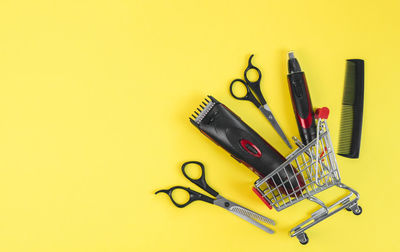 Scissors, combs and hair and ear clippers, nose clippers in a mini cart on a yellow.