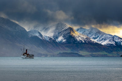 Sailboat in sea by snowcapped mountains against sky