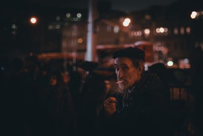 Portrait of man smoking while standing in city at night