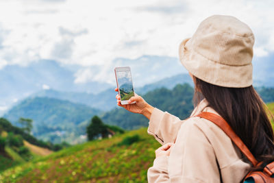 Rear view of woman drinking water while standing against mountain