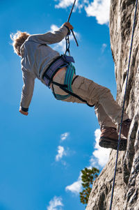 Low angle view of girl climbing on rock against sky