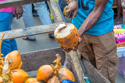 Midsection of man cutting coconut while standing at market stall