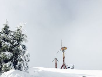 Windmill on snow covered landscape against sky