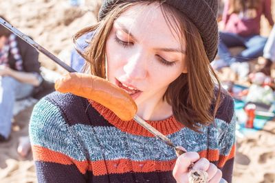 High angle view of young woman eating sausage while standing outdoors