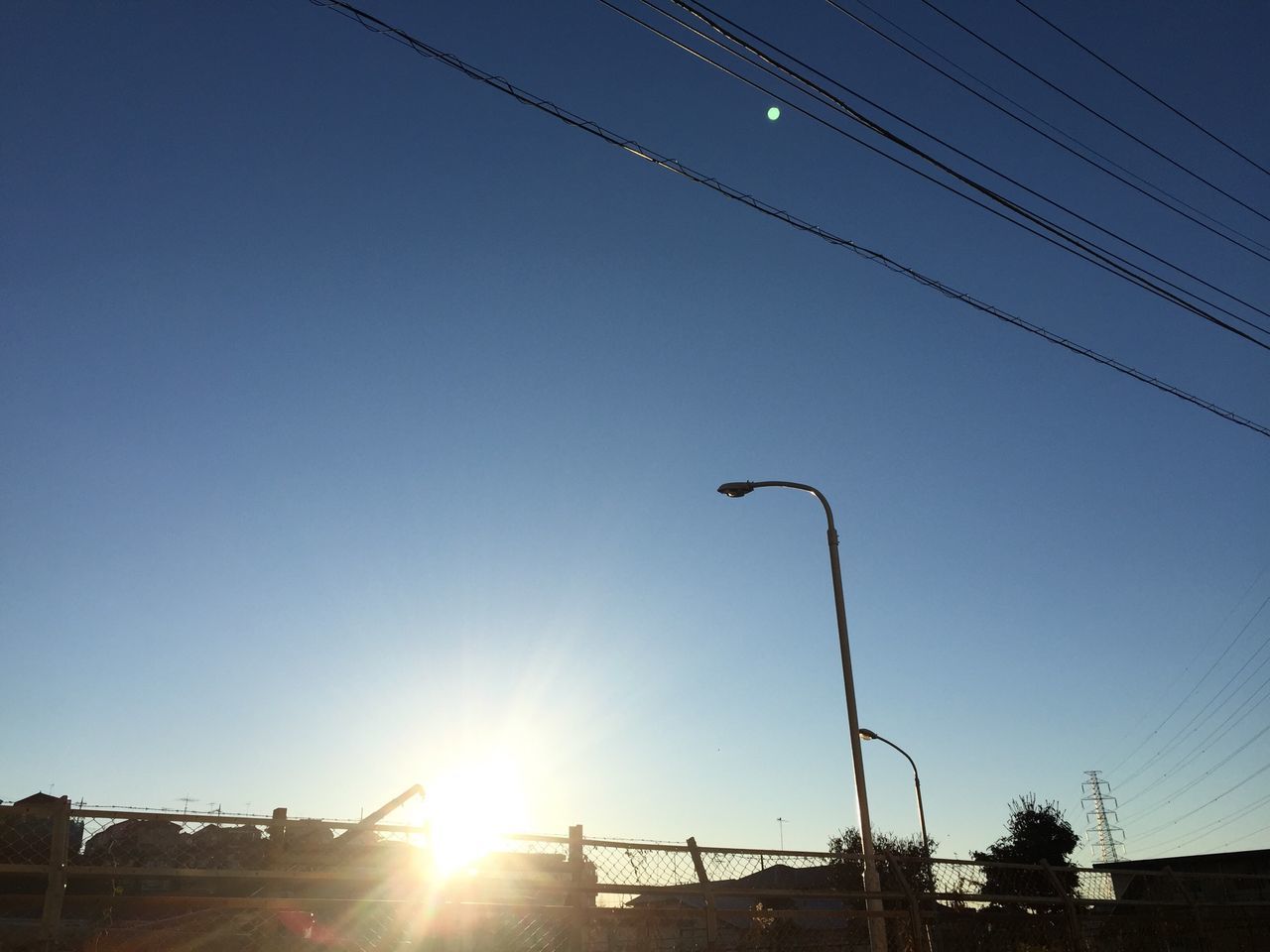 sun, clear sky, low angle view, sunlight, silhouette, sunbeam, blue, sunset, lens flare, street light, copy space, sky, built structure, power line, bright, electricity pylon, outdoors, electricity, nature, cable