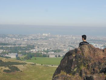 Rear view of man standing by rock over landscape against sky