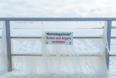 Information sign on railing by sea against sky