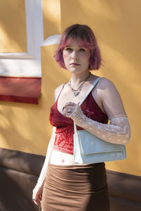 Portrait of young woman standing against wall