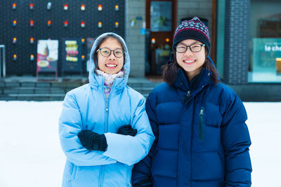 Portrait of friends standing against building during winter