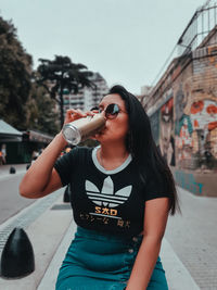 Young woman wearing sunglasses standing against sky in city