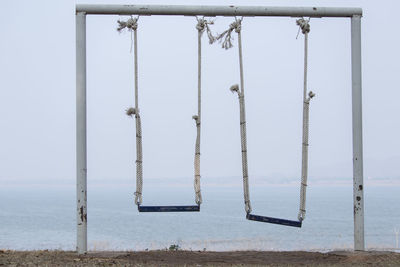 Wooden swing hanging on beach against clear sky