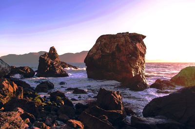 Rocks on sea shore against sky during sunset