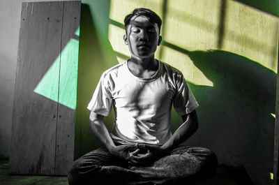 Portrait of young man sitting against wall