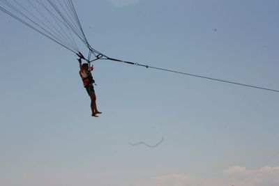 Low angle view of man hanging on rope against sky