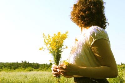 Rear view of woman holding flower against clear sky