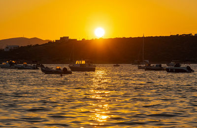 Silhouette sailboats in sea against orange sky