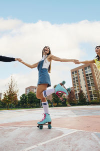 Happy woman holding hands of friends and roller skating at sports court