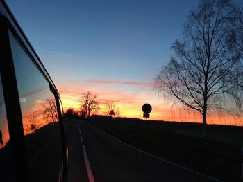 Silhouette bare trees by road against sky during sunset